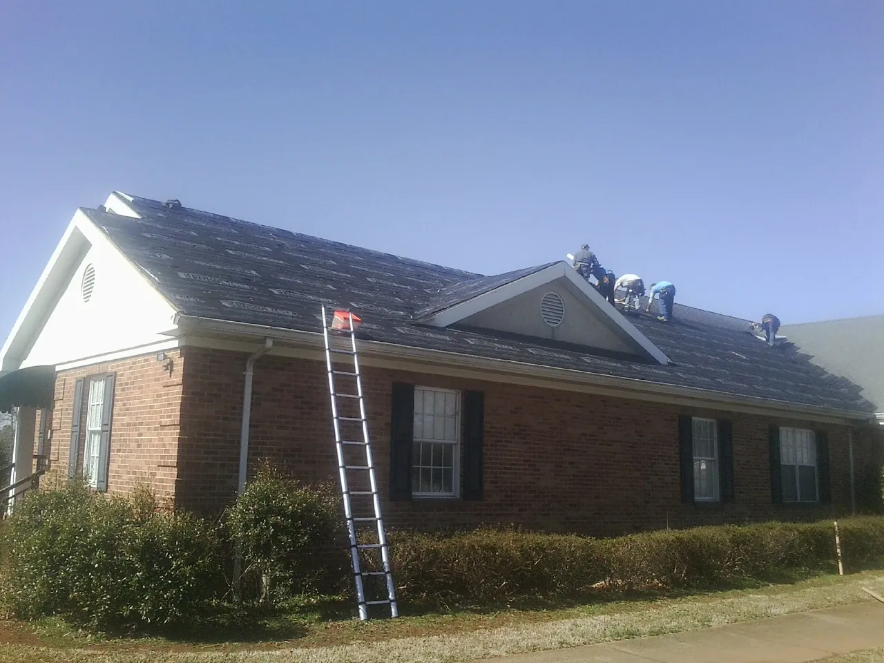 Crew tearing shingles off a brick ranch roof with a ladder set — Emergency Roof Repair work by our crew in New Park