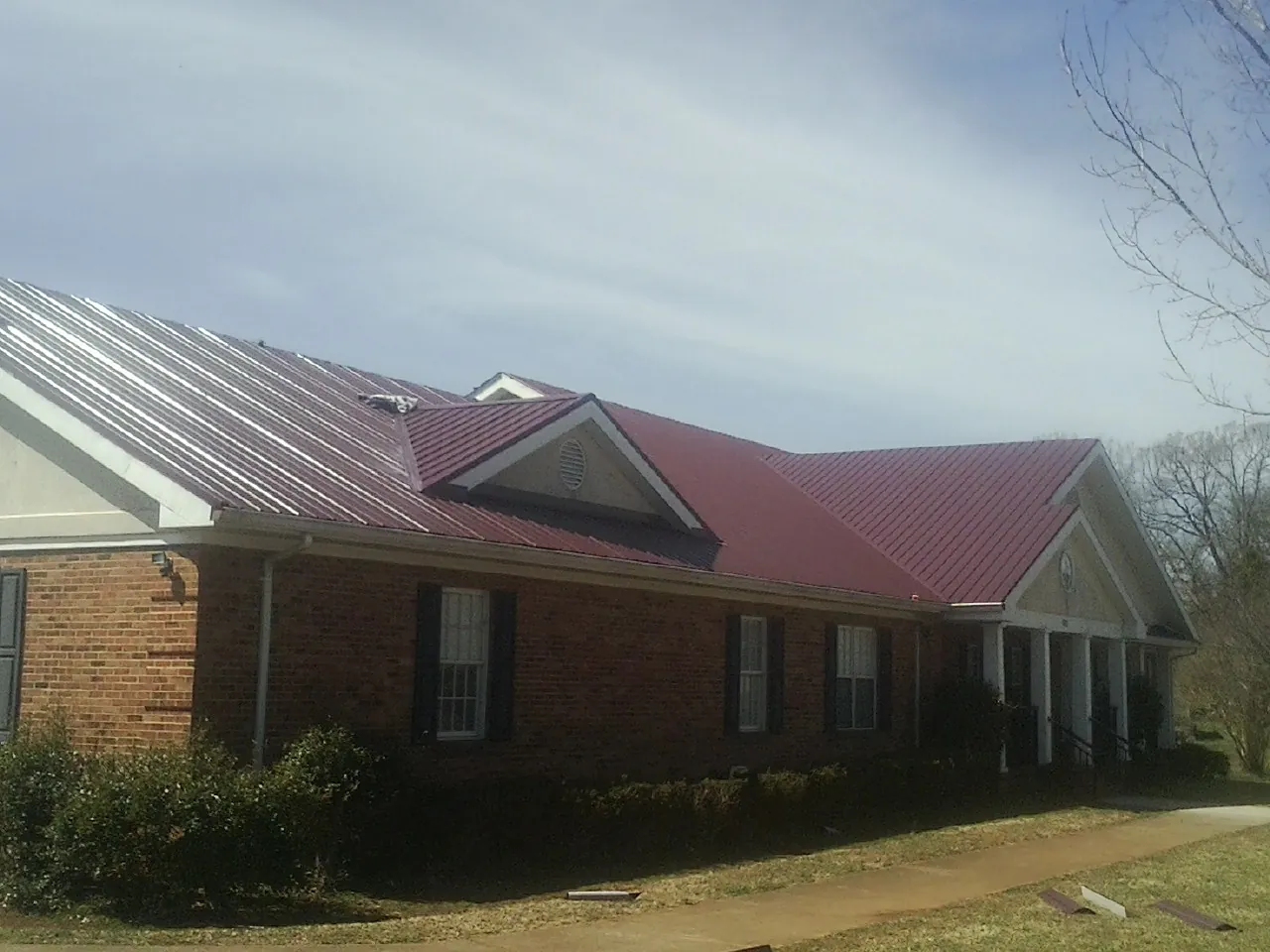 Red metal roof with gabled entries on a long brick building, from a Hail Damage Roof Repair job in New Park