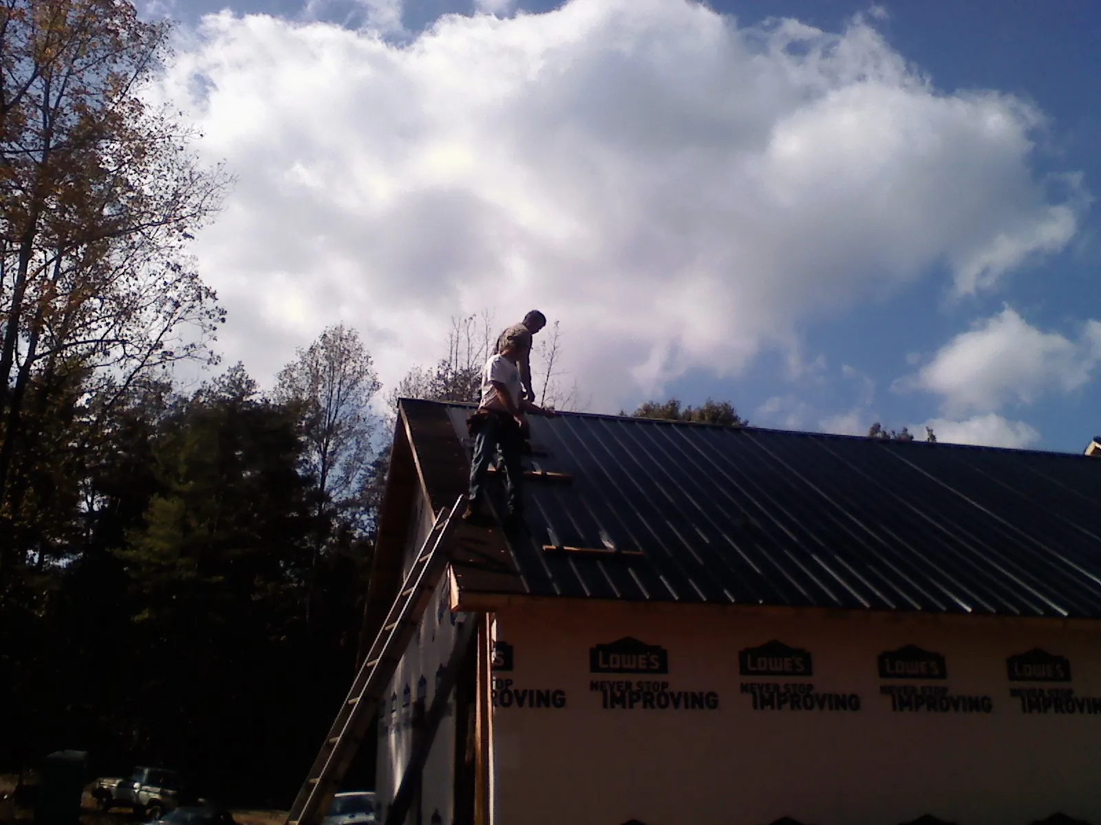 Roofer fastening dark metal panels high against a cloudy sky, from a Roof Inspection job in New Park