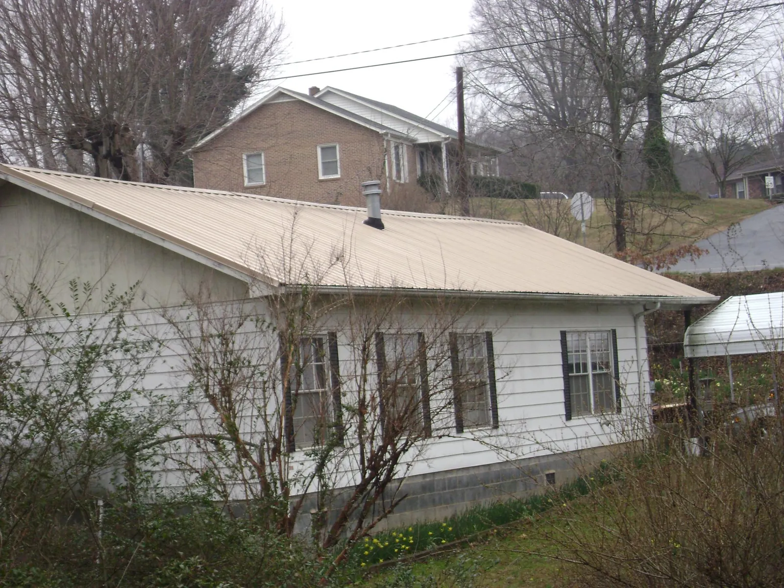 Tan metal roof on a white sided house set into a hillside — Commercial Roofing by Roofing Brothers in New Park